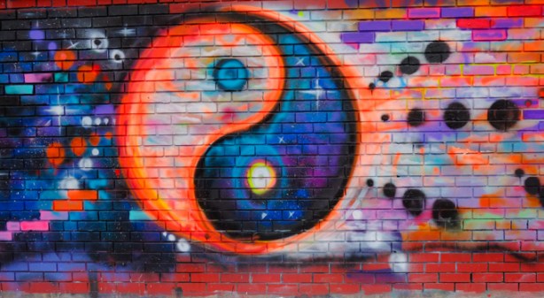 a yin and yang circle and dots mural in blues and oranges, on a brick wall,