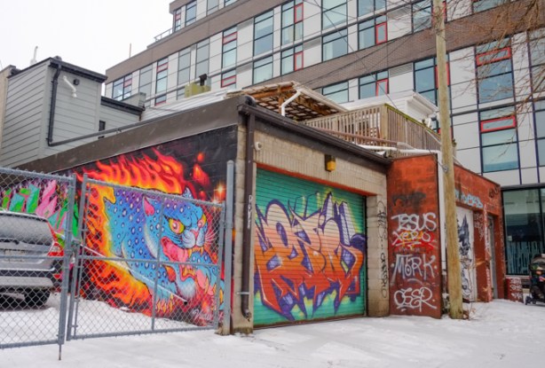 garage in laneway with street art murals on side as well as on garage door. 