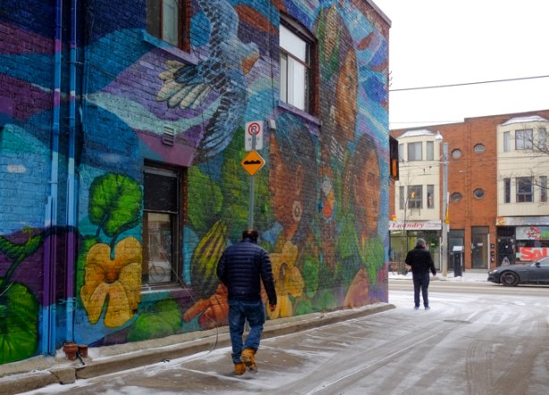 man in laneway walking past a large mural, Three Sisters, 