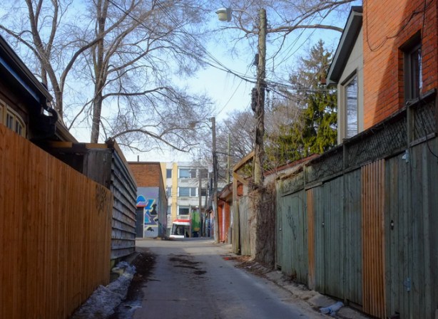 looking north up Rocco Mandalfino Lane, streetcar passing by the north end of the alley, wood fences, large trees, winter, graffiti on the garages, brick houses