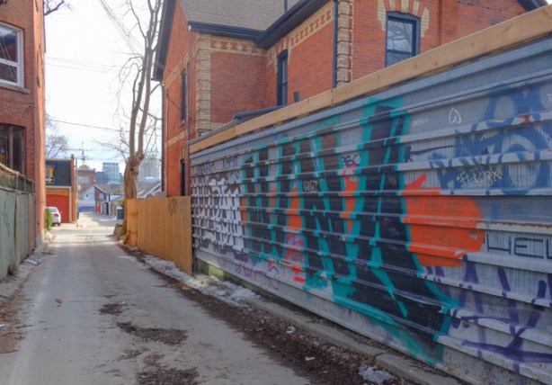 fence with graffiti and street art, lane in toronto, beside red brick house with yellow brick details, looking south in rocco mandalfino lane