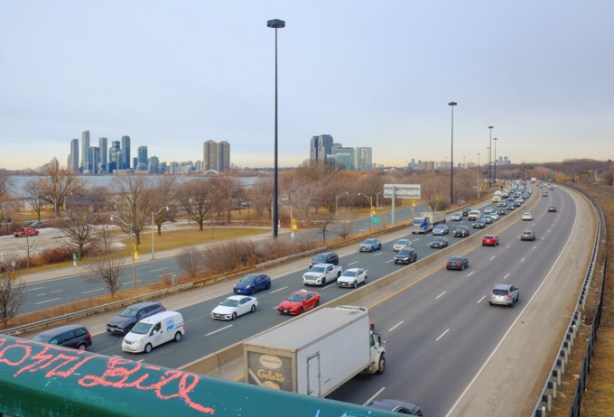 view from pedestrian bridge over lakeshore blvd and gardiner expressway, traffic on the roads, etobicoke and mississauga in the distance, lake ontario