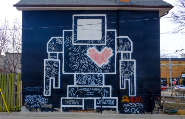a very big lovebot the robot street art, on a black building, white lines, faded red heart, on legs the words still alive are written