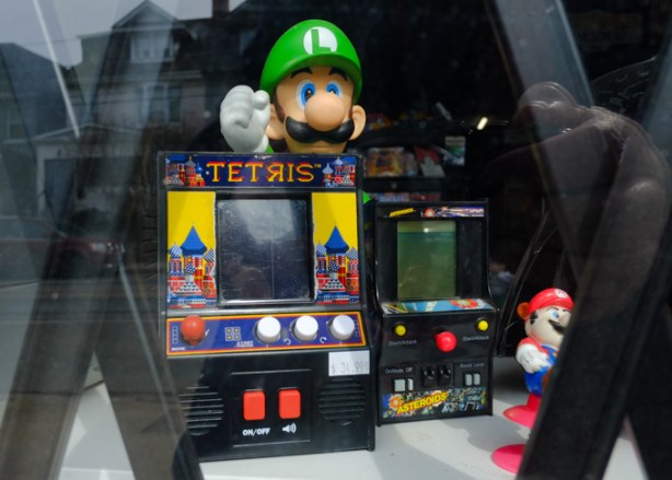 in the window of a store, a figurine of Luigi from Mario brothers, with a toy tetris game