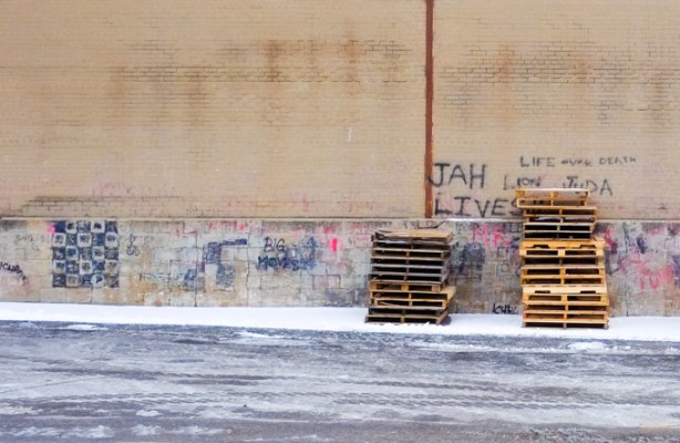 two piles of pallets sitting outside a brick building with graffiti on the walls