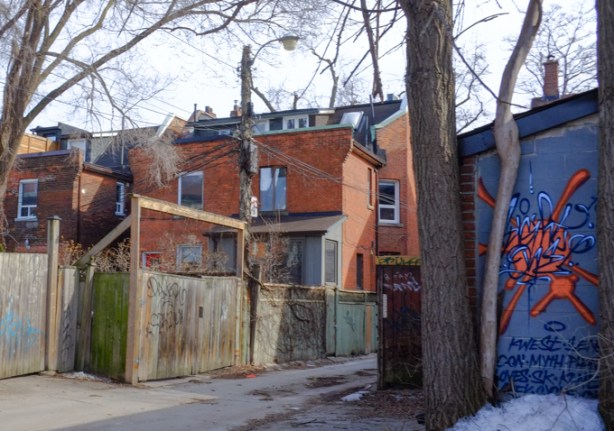 wood fences, and backs of brick houses, alley views, large trees, one small wall with street art in red and blue