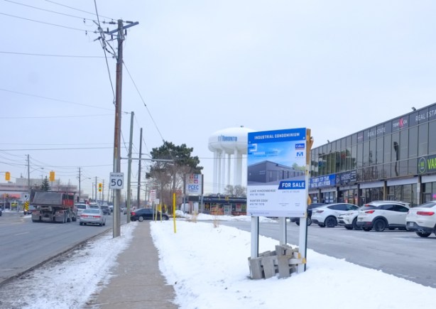 large for sale sign beside stores and businesses on warden ave., toronto water tower in the background, snow, 