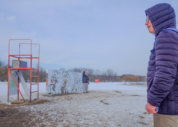 winter stations art installation, hundreds of little reflective squares that move in wind, reflecting beach and lake and sky , people looking at