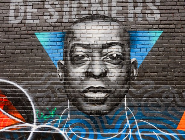 portrait of a young black man, with a triangle behind his head, in a mural in an alley