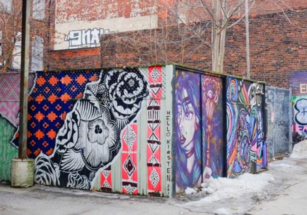 murals on a fence in an alley including one by hello kirsten, design patterns, also a woman in purple, 