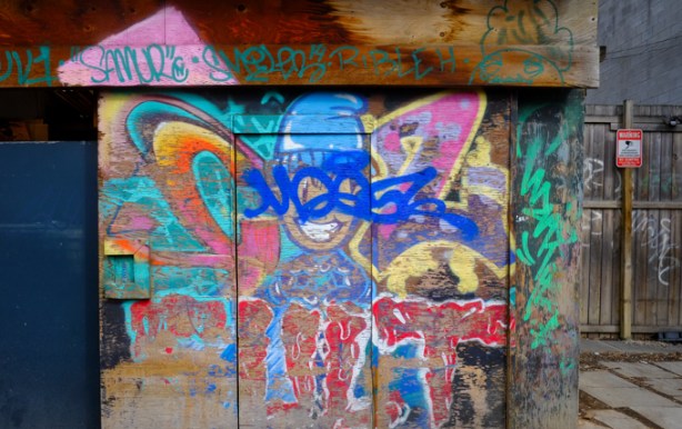 weathered street art and graffiti on a wood garage in an alley