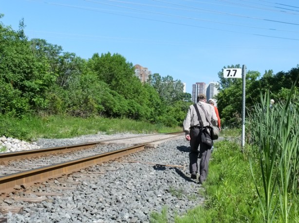 two people walking along the side of the railway tracks, apartment buildings in the background,