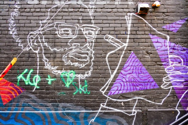 white line drawing on black line drawing of a man with glasses and a beard, mural in an alley