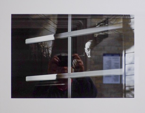 black and white photo of a man looking out a window, by David Williams, with reflections of the photographer and the wall behind