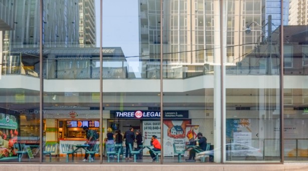 view from Cumberland Ave., into the glass wall of Cumberland Terrace, people sitting at tables for lunch, reflections of tall buildings behind 