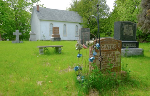 tombstones, monuments in a churchyard, with an old small concrete bench, small white wood church, Hillside church, in the background