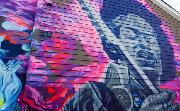 black and white image of Jimmy Hendrix singing and playing guitar, pink background, mural 