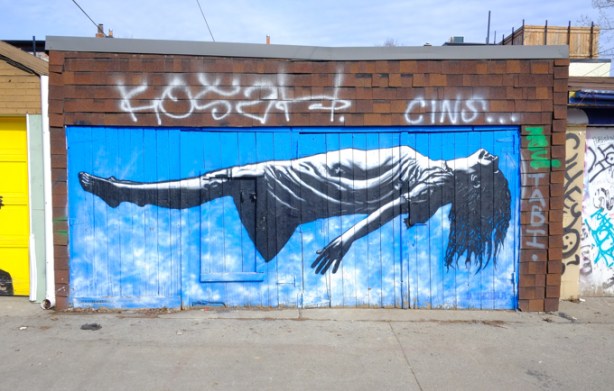 mural on an alley garage door by D.TErra stencils, a levitating woman, lying on her back up in the air, long hair hanging down.