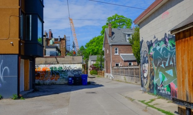 alley scene, 2 murals, a wood fence, and the back of a brick house