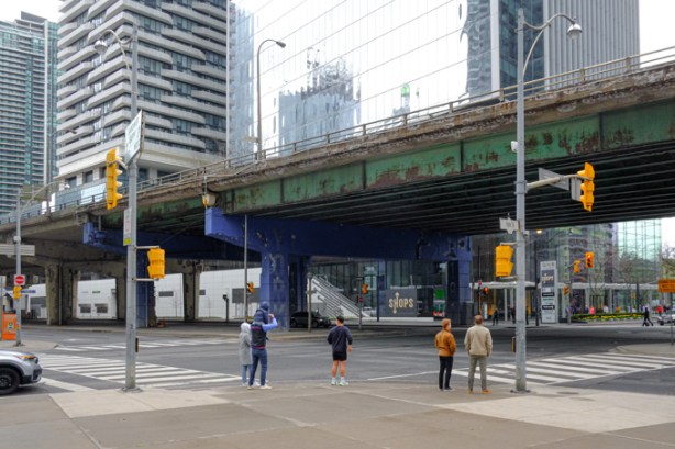 people waiting to cross Lakeshore Blvd., at traffic lights at York St., Gardiner Expressway passes over Lakeshore