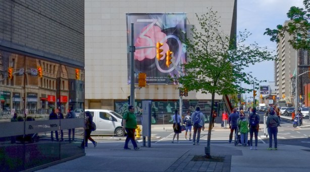 people waiting for traffic lights, before crossing St george, at bloor, by the bata shoe museum, reflections in the window of the building beside them
