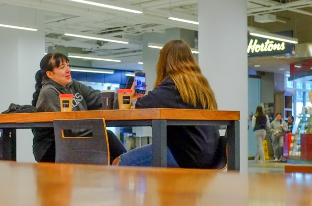 two women sharing photos that they have on their phone, sitting at TIms