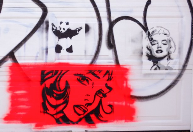 black stencil graffiti on a white garage door, portrait of Marilyn Monroe, and kung fu panda image, as well as another woman's head and face