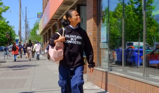 woman walking alone on sidewalk with purse over her shoulder and wearing a navy blue sweatshirt that says talentless but connected on the front of it