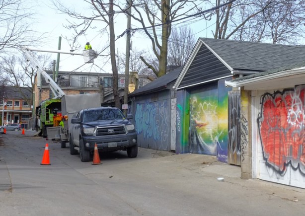 trimming trees in an alley, man in lift above the lane, truck, some garages with graffiti and street art