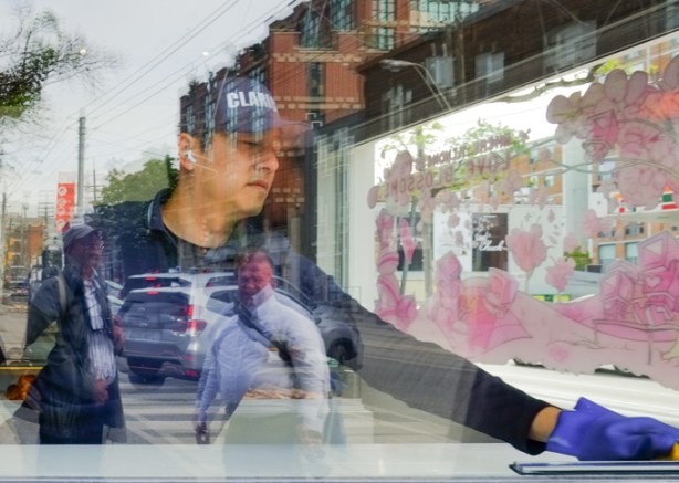 man washing inside of window, reflections of other people, cars, and buildings in the same window