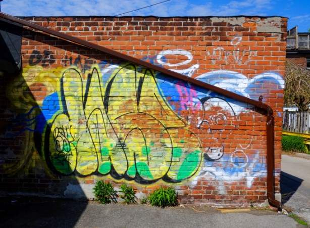 old brick wall in alley, covered with graffiti in bright colours, yellow, blue and green