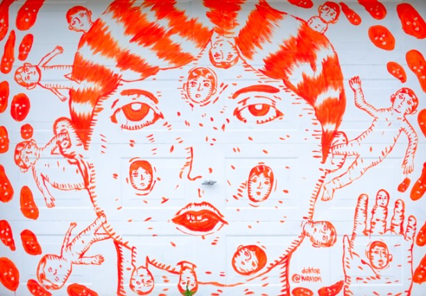 orange paint on white garage door, a large face with other smaller heads coming out of it, doktor karayom, in an alley