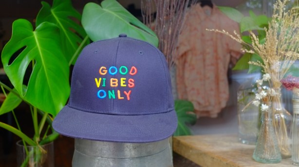 blue baseball hat in the window of a store, embroidered with the words good vibes only