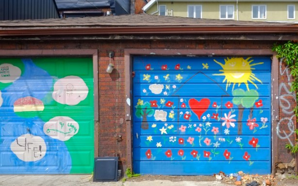garage door in alley, painted blue, with hearts and flowers on it, as well as a bright yellow sun in the corner