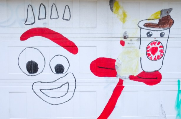 artwork on a white garage door, face, red arm, hand out, holding piccachu and a coffee cup with a face on it 