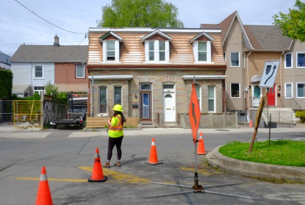 worker in yellow vest and hard hat controlling traffic on Shaw street because part of road is closed, rowhouses behind, 