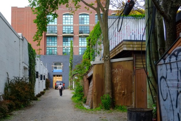a woman walks down an alley towards a car parked by a garage