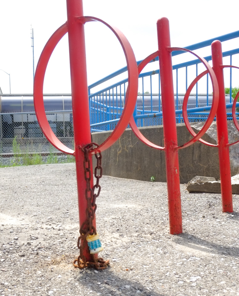 three toronto bike lock rings, painted red, one with a rusty chain and combination lock still on it.