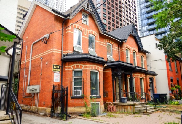 set of 3 rowhouses, red brick, bay and gable, with taller apartment buildings and condos behind them