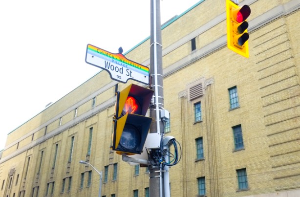 street sign for Wood st., with header of Church Wellesley village in rainbow stripes, old Maple Leaf Gardens in the background