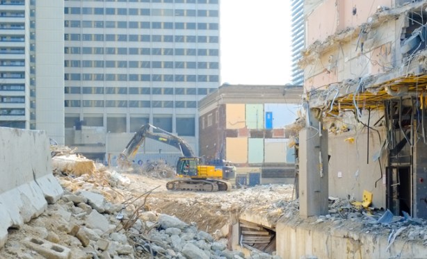 yellow digger, at construction site where a building is being demolished, revealing older interior walls painted in bright colours