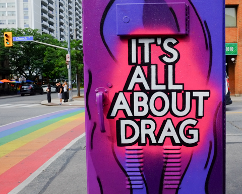 sidewalk traffic box painted in blues and purples with large text that says It's all about drag