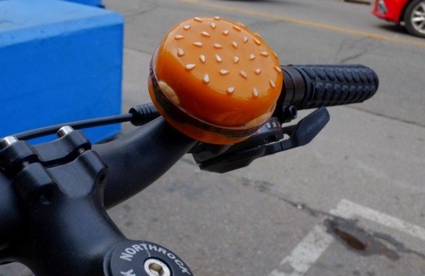 bell on the handle bar of a bike, shaped like a cheeseburger with a sesame seed bun