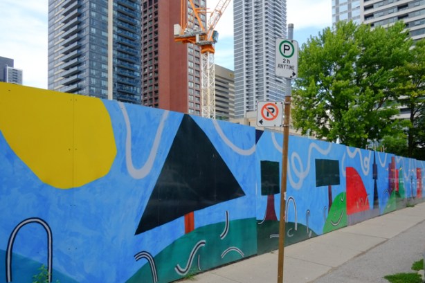 hoardings around a construction site at Howard & Sherbourne, design by Sarah Klawiter, abstract shapes that look a bit like a city scene, with trees and grass, as drawn by a child