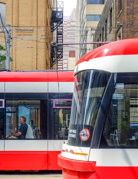 a man sits in a TTC streetcar in downtown Toronto as another streetcar passes it, going in the opposite direction