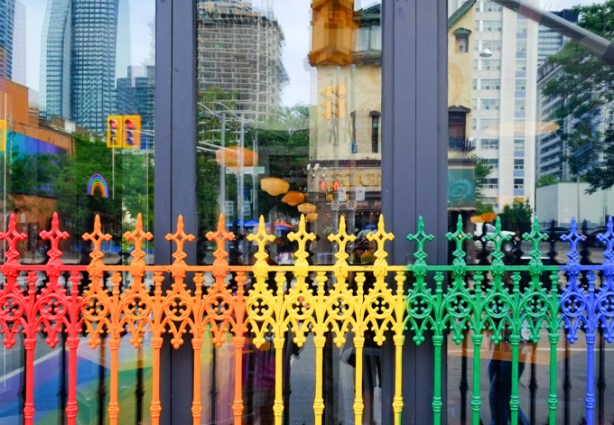 metal fence in front of store window painted in rainbow colours, reflections in the glass