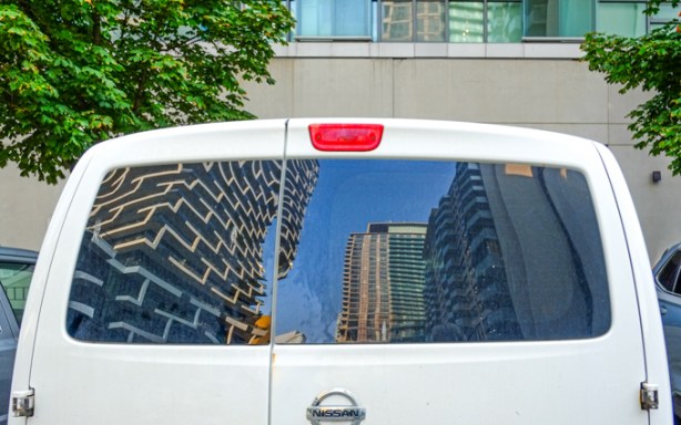 reflections of new glass and steel condos in the back window of a small white van or truck