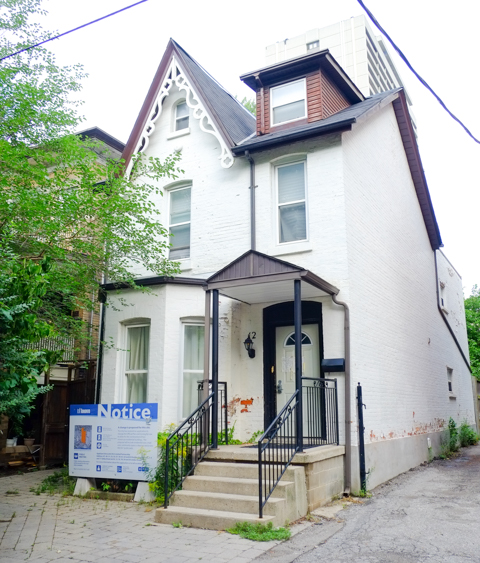 older white two storey house, with development notice sign on the front lawn
