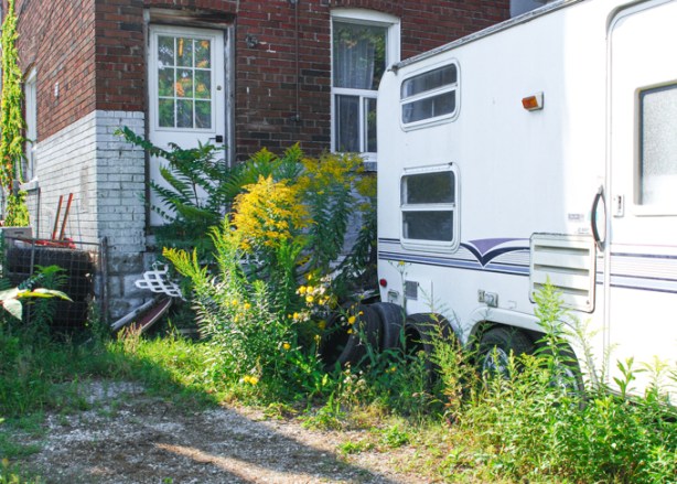 white camper of RV parked behind house, goldenrod weeds growing by the back door.