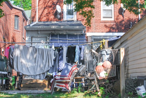 backyard alley view, lots of stuff, including a shopping cart full of basketballs and soccer balls, chairs, sheets and clothes hanging from a yellow rope clothes line